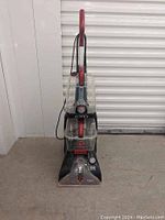 Front view of Hoover Power Scrub Elite carpet cleaner showing transparent water tanks, red handle, and control dial.