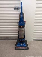 Full front view of the blue Hoover Windtunnel upright vacuum cleaner upright against a wall.