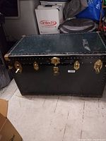 Side view of large black vintage steamer trunk with brass latches and corner caps placed on a floor.