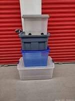 Stack of 4 assorted plastic tote bins with lids, showing frontal view of sizes and colors, placed in storage locker environment.