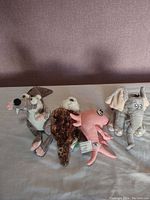 Four plushies on beige surface against textured brown background, includes Scrat, Horton, pink fish and brown bird