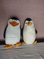 Two Madagascar penguin plush toys standing side by side, showing overall sizes and details.