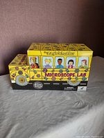 Front and side view of original Magic School Bus Microscope Lab toy box featuring cartoon bus shape and characters.