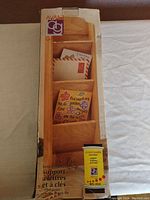 Photo of the wooden mail and key holder rack in its original box showing the front view with mail in the slots and the yellow product label.