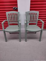Front view of two greenish-gray plastic lawn chairs side by side showing lattice backs and broad armrests.
