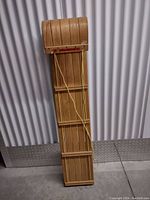 Full vertical view of the wooden child's sled showing slatted wood design with front curved upward and yellow pull rope.