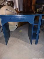 Front-left angled view of the small blue computer desk showing the drawer and shelving on the right side.