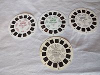 Four Viewmaster reels displayed on a fabric surface. Three Batman reels and one Mickey Mouse reel visible, showing the small transparent 3D slide windows and printed labels on the flat discs.