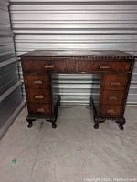 Front view of vintage wooden writing desk showing drawer layout and claw-foot legs.