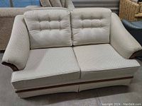 Front-facing view of white loveseat with button-tufted back cushions and wood trim along arms and base.