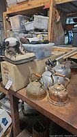 Shelving and table showing vintage tea kettles, hiking boots, plush panda, and model sailboat box.