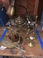 Wide view of the brass items showing candle holders, deer figures, lamp, urn, mirror, and brush on table.