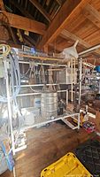 Wide view of brewing setup on metal frame with kegs, hoses, and tools in a wooden workshop environment