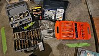 Multiple cases displayed on floor showing a variety of drill bits and accessories, including gold-colored drill bits and a green rotary tool.