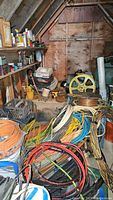 Overview of attic storage containing multiple coiled wiring cables, vintage metal tank, shelves with chemicals and paint supplies