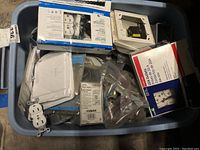 Blue plastic bin filled with assorted electrical supplies including white duplex outlets, outlets in boxes, plastic covers, and additional electrical components.
