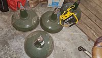 Three green pendant light shades and one mounted with yellow portable work light on concrete floor
