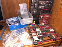 Overview photo showing multiple plastic storage containers filled with jewelry making supplies including beads and fasteners on a wooden surface.