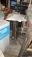 Full view of stainless steel propane powered porch heater showing the canopy and base in a storage setting.