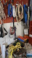 Full view of ropes, straps, and cords hanging on wall hooks and stored below, showing variety of colors and types.