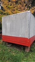 Side view showing large rectangular container painted white on top and orange on bottom with riveted panels.