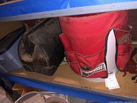 Shelf with black tool bag and red Buck Boss bucket tool apron with external pockets containing some hand tools
