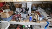 Shelf with multiple plastic bins, metal toolbox, tape measures, metal straps, conduit, and lubricant container.