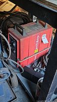 Red PowCon welding unit under workshop bench with cables coiled on top