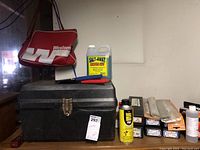 Various welding related supplies including a toolbox, a red Western branded bag, a can of gun cleaner, and multiple boxes of alloy rods on a shelf.