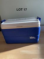 Large blue Igloo cooler with white lid and drain plug on wooden floor.