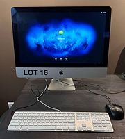 Front view of Apple iMac desktop powered on, with wireless keyboard and wired mouse on desk