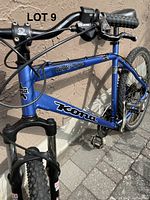Close-up of the blue Kona Cinder Cone frame with branding on the top and down tubes, showing handlebars and front forks locked in position.