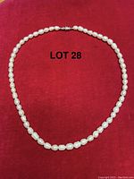 Full view of an 18 inch pearl necklace laid out on a red surface, showing the complete string and clasp.