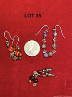 Photo shows three pairs of sterling silver dangle earrings on a red background with a quarter for size. The pairs include orange amber beads, blue moonstone and pink crystals, and red garnet beads.