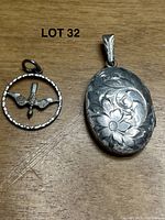 Photo of the peace dove pendant and engraved oval silver locket side by side on a wooden surface