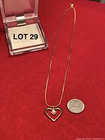 Full view of the gold chain with heart-shaped diamond pendant next to a quarter for size reference and the display box.