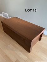 Wooden storage bench closed on hardwood floor, rectangular shape, dark finish.