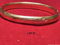 Front view of small gold hinged bangle bracelet on red background