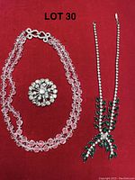 Photo of three vintage jewelry items on red background: clear crystal bead necklace, round rhinestone pin, and green rhinestone necklace
