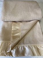 Folded oatmeal wool blanket showing satin binding and texture of the wool.