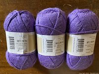 Three violet balls of yarn lined up on a wooden surface