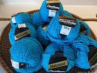 Basket holding 12 balls of bright turquoise nubbly textured yarn labeled 'Malicieuse' by Chat Botte.