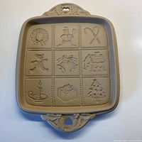 Full view of rectangular ceramic baking plate with 9 sectioned festive relief designs and two decorative handles.