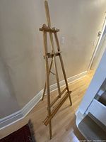 Full view of the wooden easel showing its tripod stance and overall height against a wall.