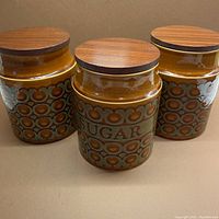 Three ceramic canisters with rich cinnamon brown background and grey circular motifs, each topped with wooden lids