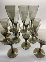 Overall collection of 13 smokey grey glasses showing different shapes and sizes representing red wine, white wine, aperitif glasses, and champagne bowls.