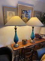 Full view of the pair of blue ceramic table lamps on a wooden surface with shades lit.