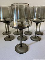 Front view of 8 smokey grey wine glasses arranged in a group showing their bowl and stem design.
