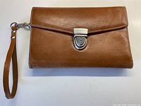 Clutch closed showing tan leather exterior with silver-tone clasp and attached wrist strap.