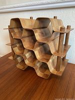 Front and side view of the bentwood checkerboard patterned wine rack showing the three horizontal grooves for holding wine bottles and the wooden pegs on the side.
